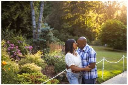 This lovely photo of Nikki and Leon beautifully captures a romantic summer moment at Chateau Ste. Michelle. Bathed in golden-hour light, the couple shares a tender kiss surrounded by lush gardens, blooming flowers, and towering trees—a perfect blend of elegance and nature. Their coordinated casual-chic outfits add a relaxed charm to the setting, making this an ideal highlight for a couples session