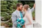 Bride and groom sharing an intimate moment on a white wooden bridge surrounded by greenery, with the bride holding a cascading bouquet of turquoise, blush, and white flowers.