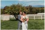 Bride and groom share a quiet moment in a sunny field at Eagle Mountain country venue in Arlington, with mountains in the background and a colorful wildflower bouquet in the bride's hands.