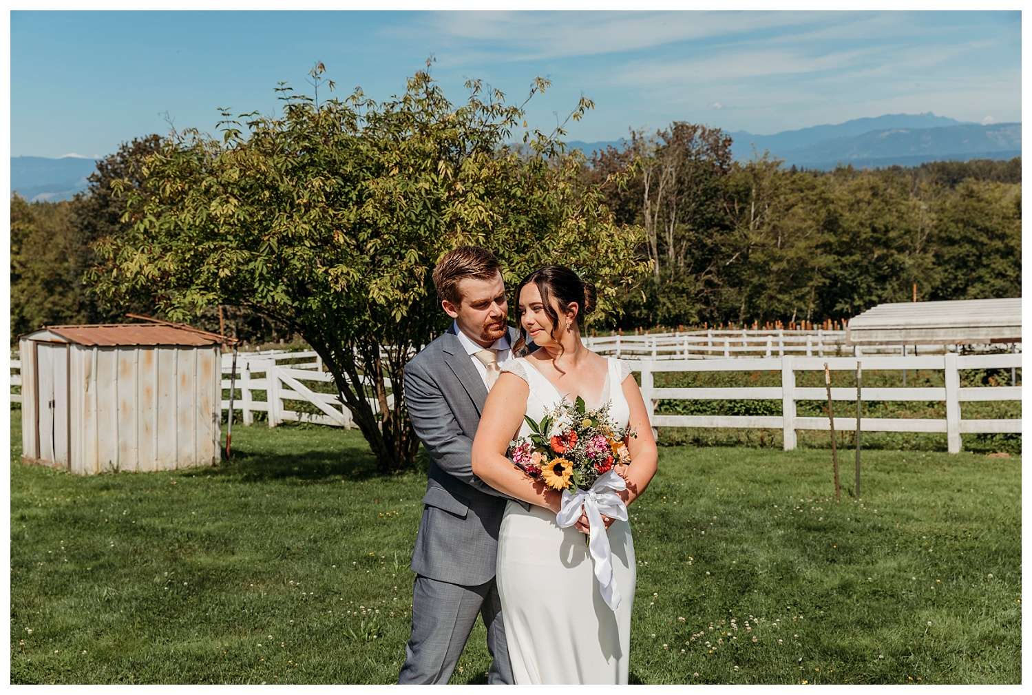 Bride and groom share a quiet moment in a sunny field at Eagle Mountain country venue in Arlington, with mountains in the background and a colorful wildflower bouquet in the bride's hands.