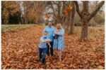 "Family of four smiling and posing together under a canopy of autumn leaves during a Fall Treeline Mini Session in Snohomish, Washington."