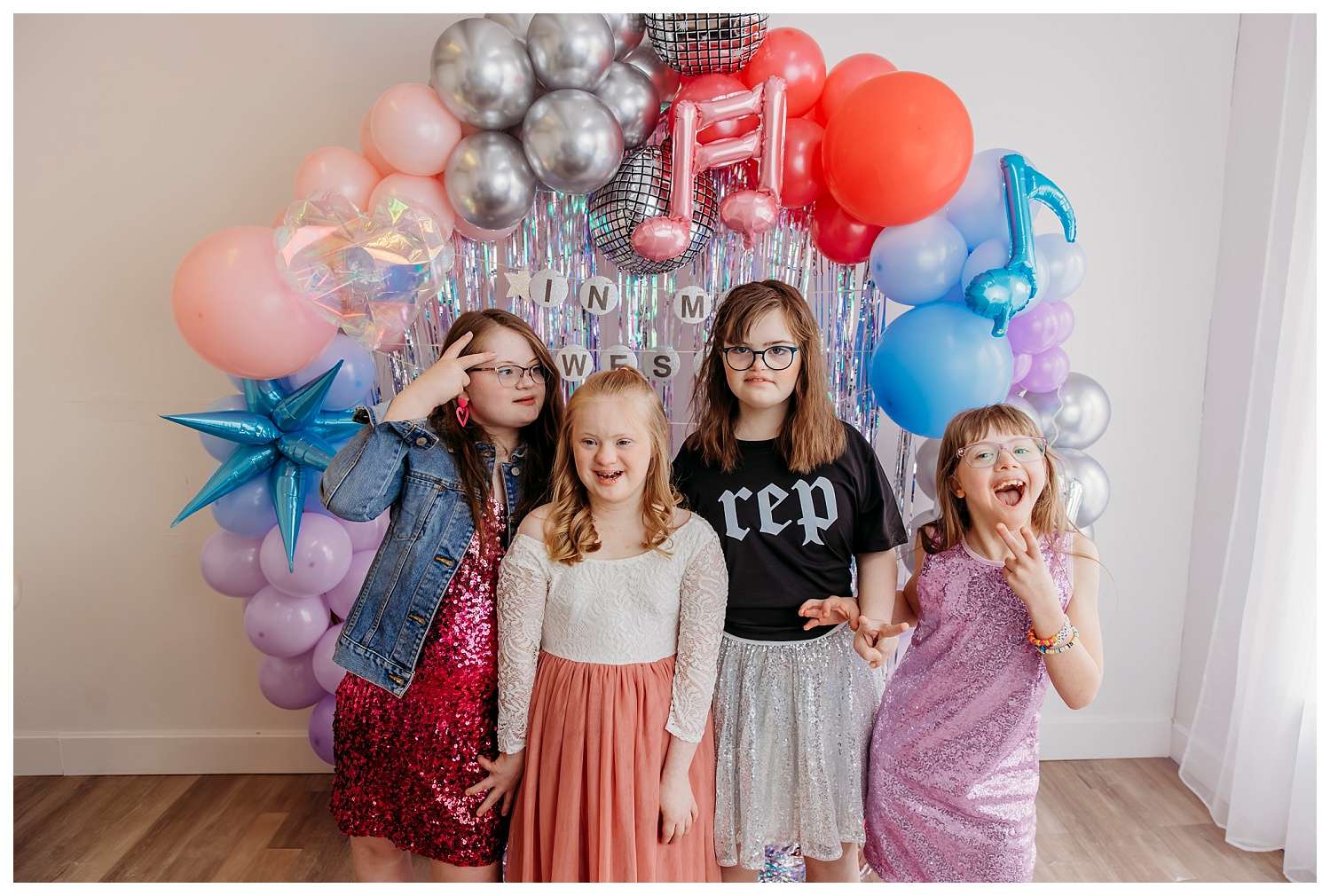 Children with Down syndrome dressed in colorful, sparkly outfits inspired by Taylor Swift’s Eras Tour, posing joyfully with microphones, sunglasses, and themed props in a bright, glittery setup at a downtown Everett photo studio for World Down Syndrome Day mini sessions.