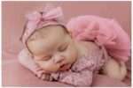 Three-week-old newborn girl named Sarah wrapped in soft pink and golden yellow blankets, peacefully sleeping in a cozy camping-themed setup with pinecones, a mini campfire, and a small Bigfoot plush, creating a whimsical outdoor adventure scene.
