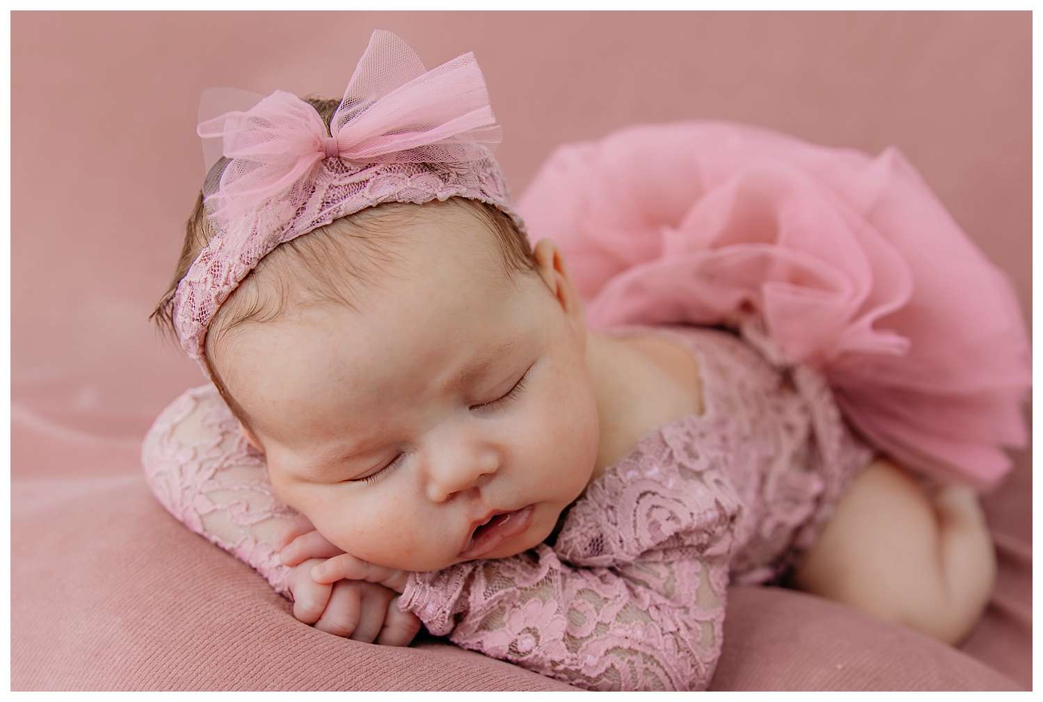 Three-week-old newborn girl named Sarah wrapped in soft pink and golden yellow blankets, peacefully sleeping in a cozy camping-themed setup with pinecones, a mini campfire, and a small Bigfoot plush, creating a whimsical outdoor adventure scene.