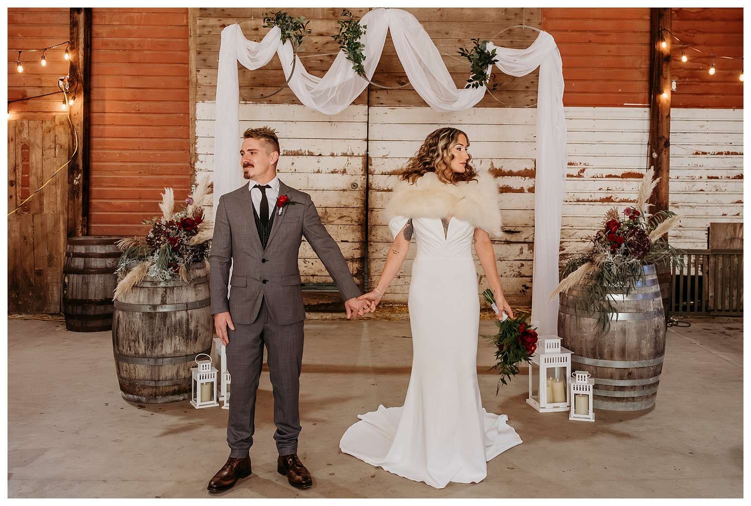 Bride wearing a long-sleeved lace gown and faux fur shawl, holding a bouquet of seasonal winter florals.