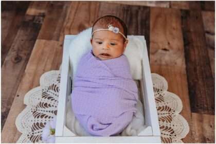 Newborn baby girl wrapped in soft pink fabric wearing a long knit hat, sleeping peacefully in a modern studio setup