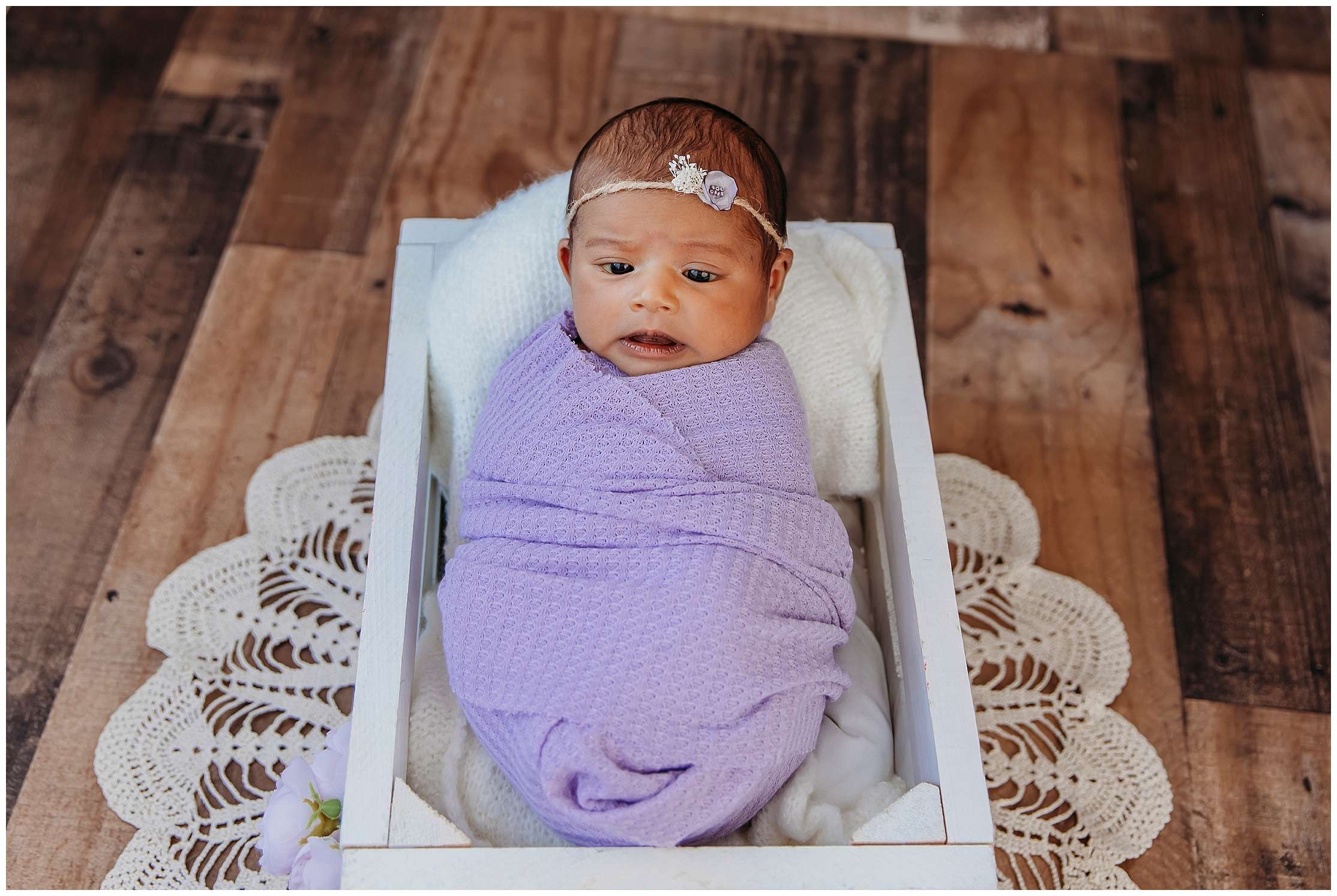 Newborn baby girl wrapped in soft pink fabric wearing a long knit hat, sleeping peacefully in a modern studio setup