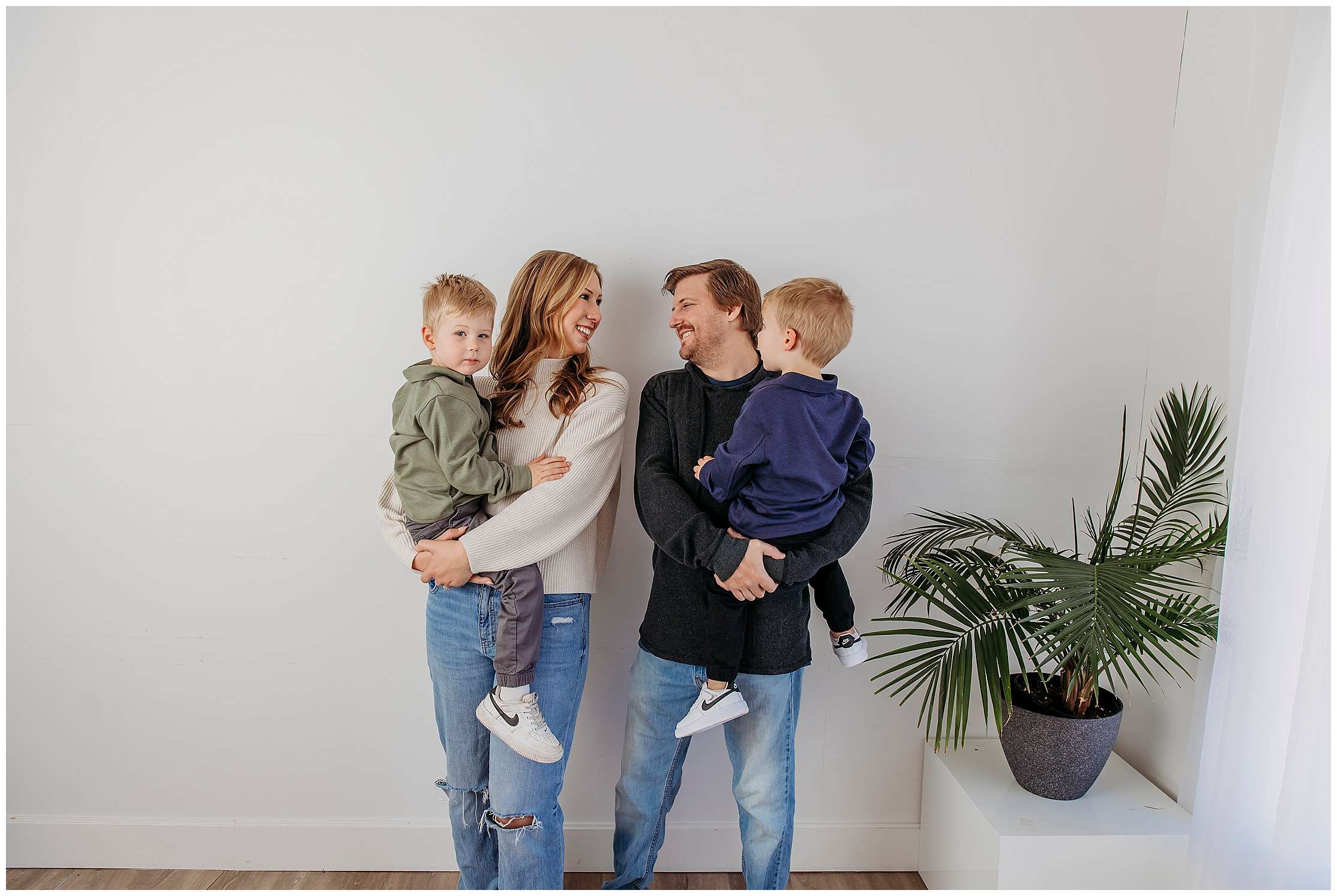 A smiling family of four poses together in a studio with their two fluffy Pomeranian dogs, sharing a warm and joyful moment.