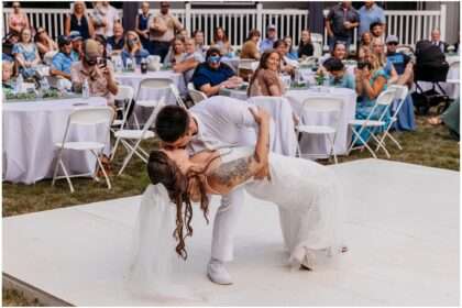 Bride and groom in white attire walking hand in hand through a grassy field during their outdoor wedding portraits, surrounded by natural greenery.