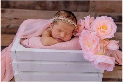Newborn baby girl sleeping in a pink bucket surrounded by white and cream flowers, styled with soft fabrics and a Hello Kitty-inspired theme.