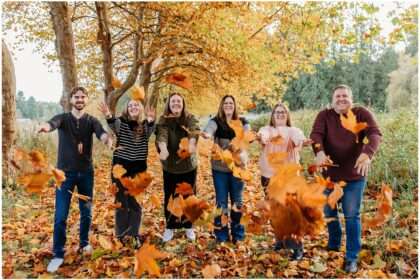 Family walking together under a tree-lined path covered in vibrant orange and yellow fall leaves during a mini photo session in Snohomish.