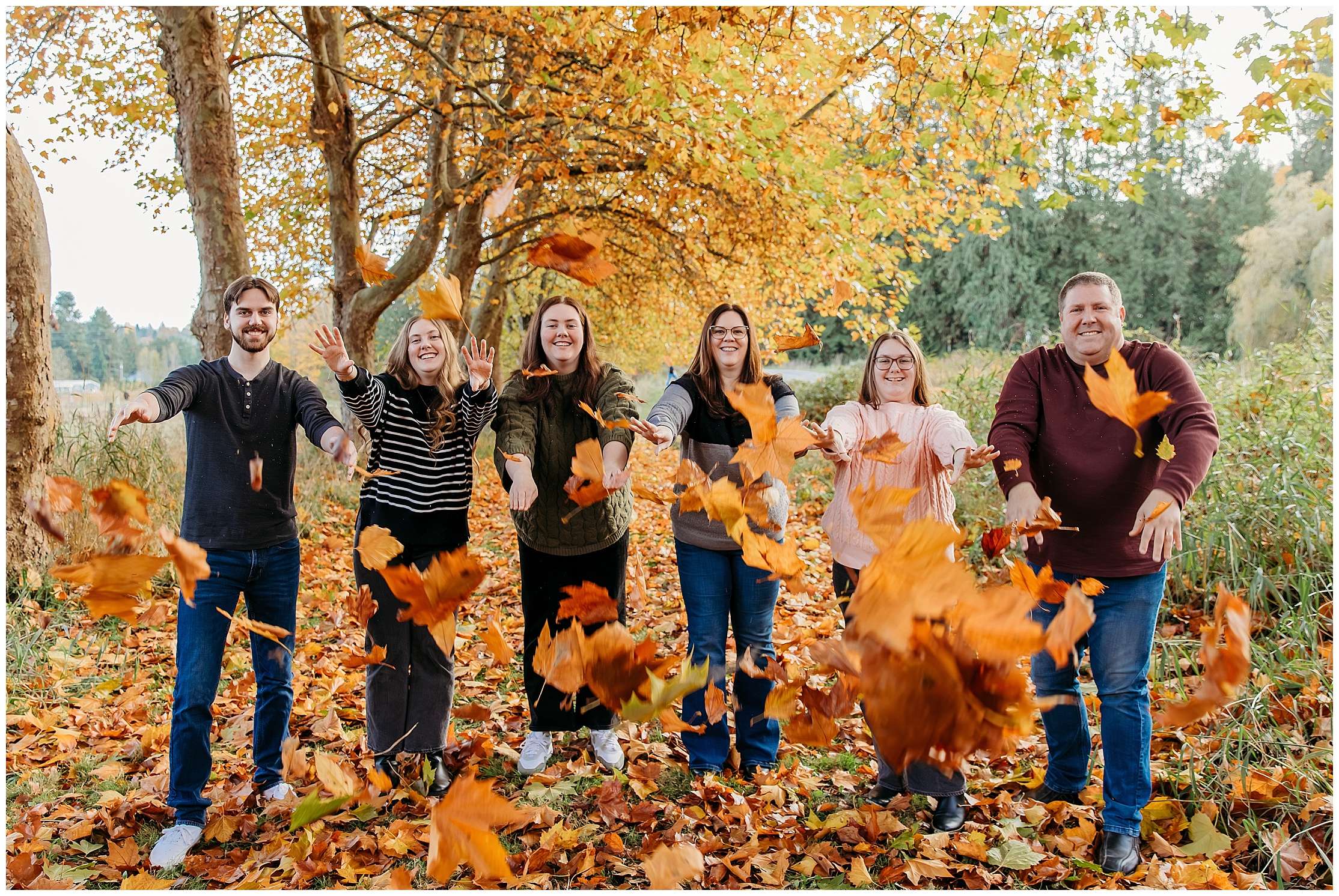 Family walking together under a tree-lined path covered in vibrant orange and yellow fall leaves during a mini photo session in Snohomish.