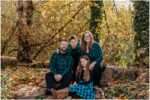 Family of four walking hand in hand on a wooden bridge at Bothell Landing in Bothell, Washington, during a November fall mini session surrounded by golden autumn leaves.