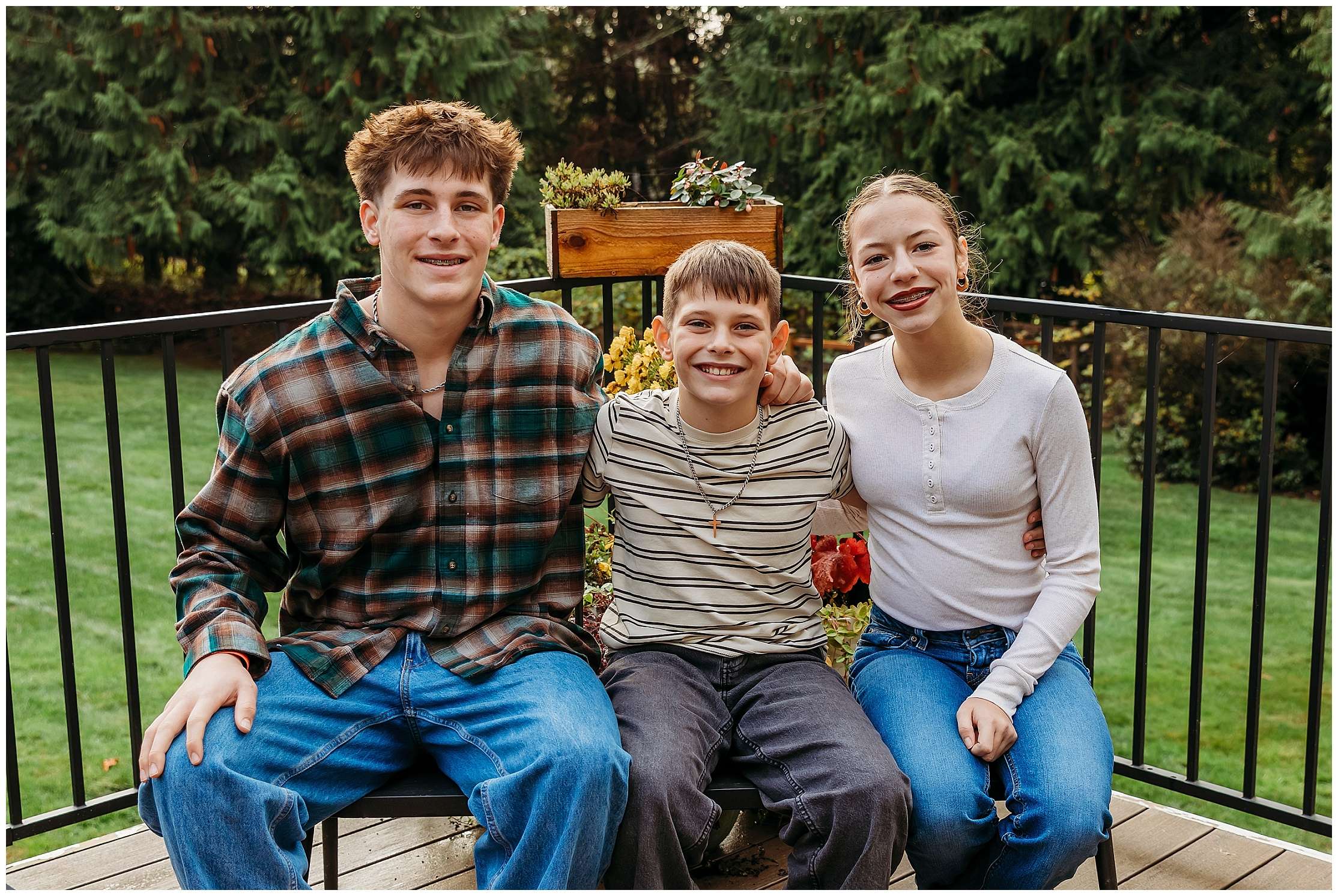 Family of five smiling together outdoors in their front yard during autumn with golden November light and evergreen trees in the background.
