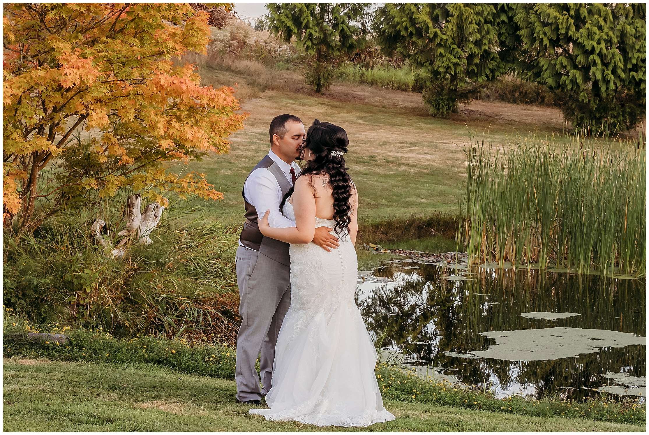 Bride and groom standing by garden pond with waterfall surrounded by lush greenery and flowers at Nature’s Connection wedding venue