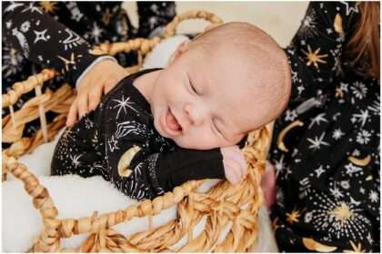 Twin toddler sisters holding their newborn baby sister Hazel, wearing matching black outfits with star patterns, showing mixed emotions during a sibling photo session
