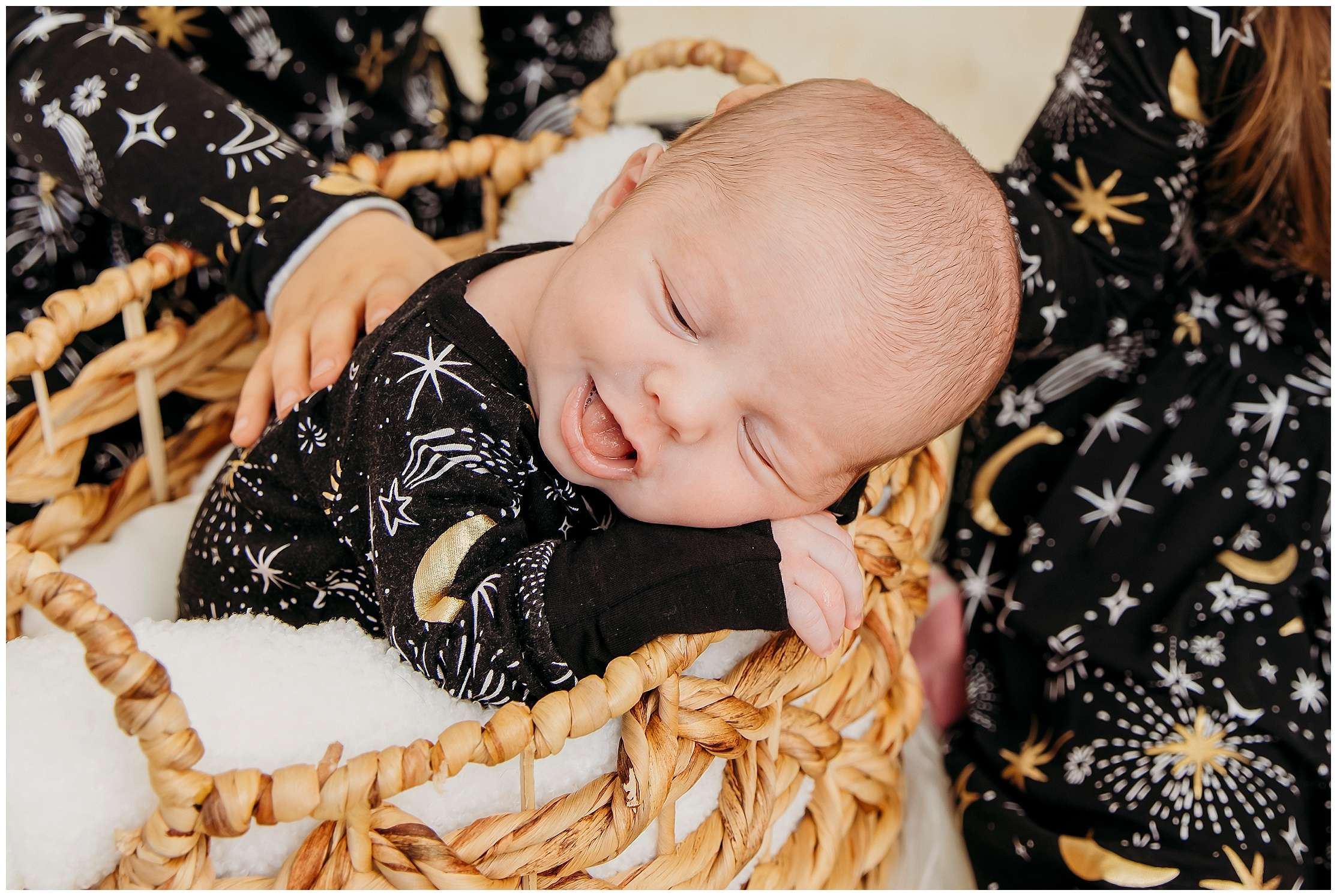 Twin toddler sisters holding their newborn baby sister Hazel, wearing matching black outfits with star patterns, showing mixed emotions during a sibling photo session