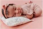 7-day-old newborn baby girl Eliana wrapped in a soft pink swaddle holding a small teddy bear during her newborn mini session in studio.