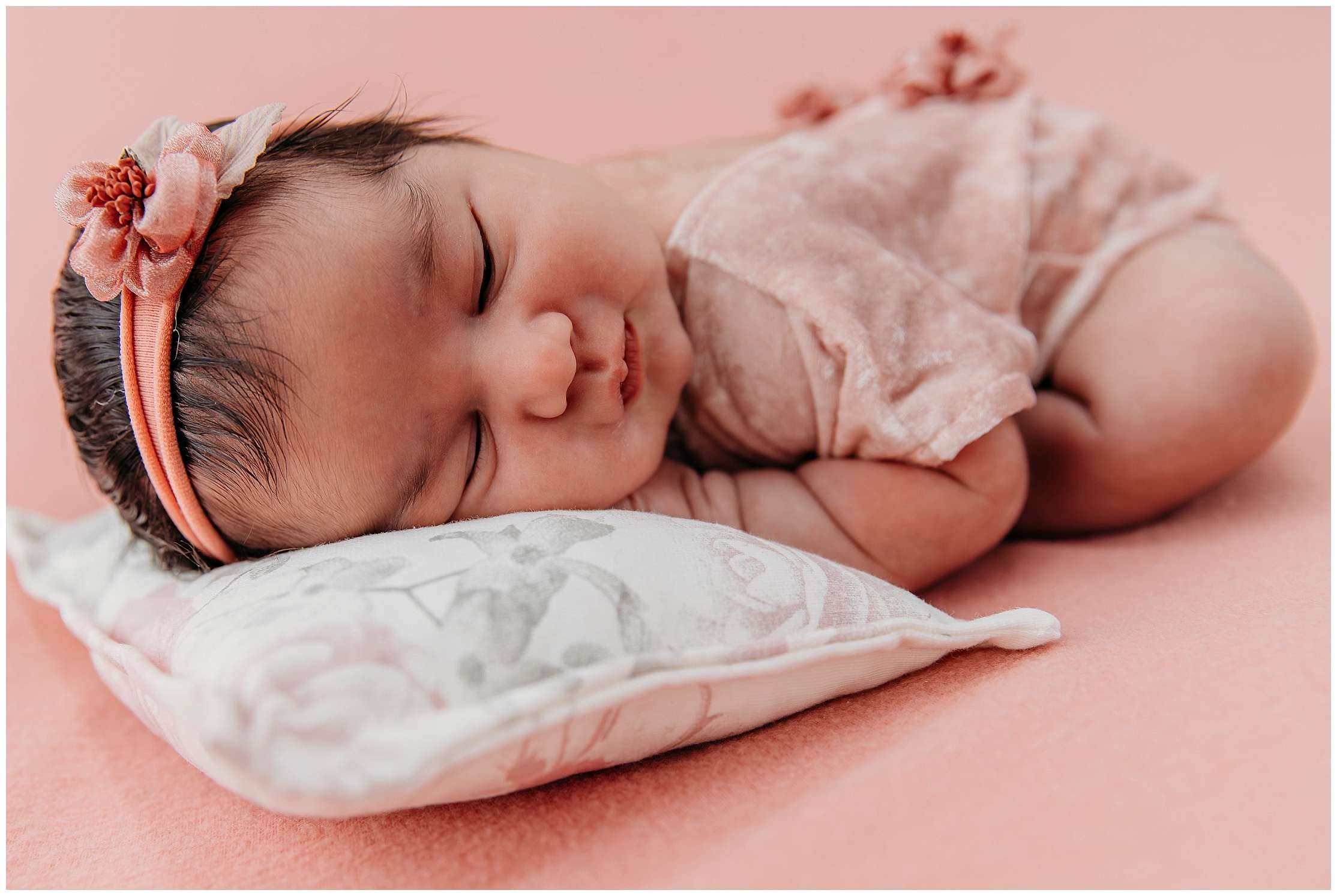 7-day-old newborn baby girl Eliana wrapped in a soft pink swaddle holding a small teddy bear during her newborn mini session in studio.