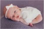 Newborn baby girl Elliana posed in a soft cream wrap with a white bow during her Downtown Everett studio newborn session.