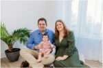 Young family sitting together in a bright Downtown Everett photography studio with their smiling 4 month old baby girl dressed in pink.