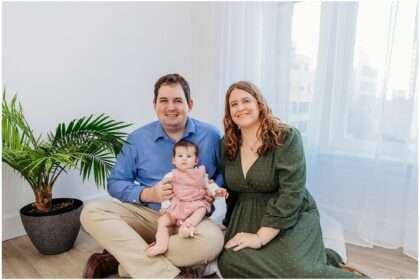 Young family sitting together in a bright Downtown Everett photography studio with their smiling 4 month old baby girl dressed in pink.