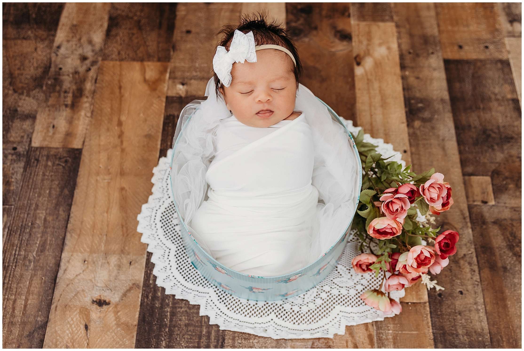 Newborn baby girl wrapped in white fabric during a Downtown Everett Studio newborn session, posed inside a floral keepsake box with soft pink flowers nearby.