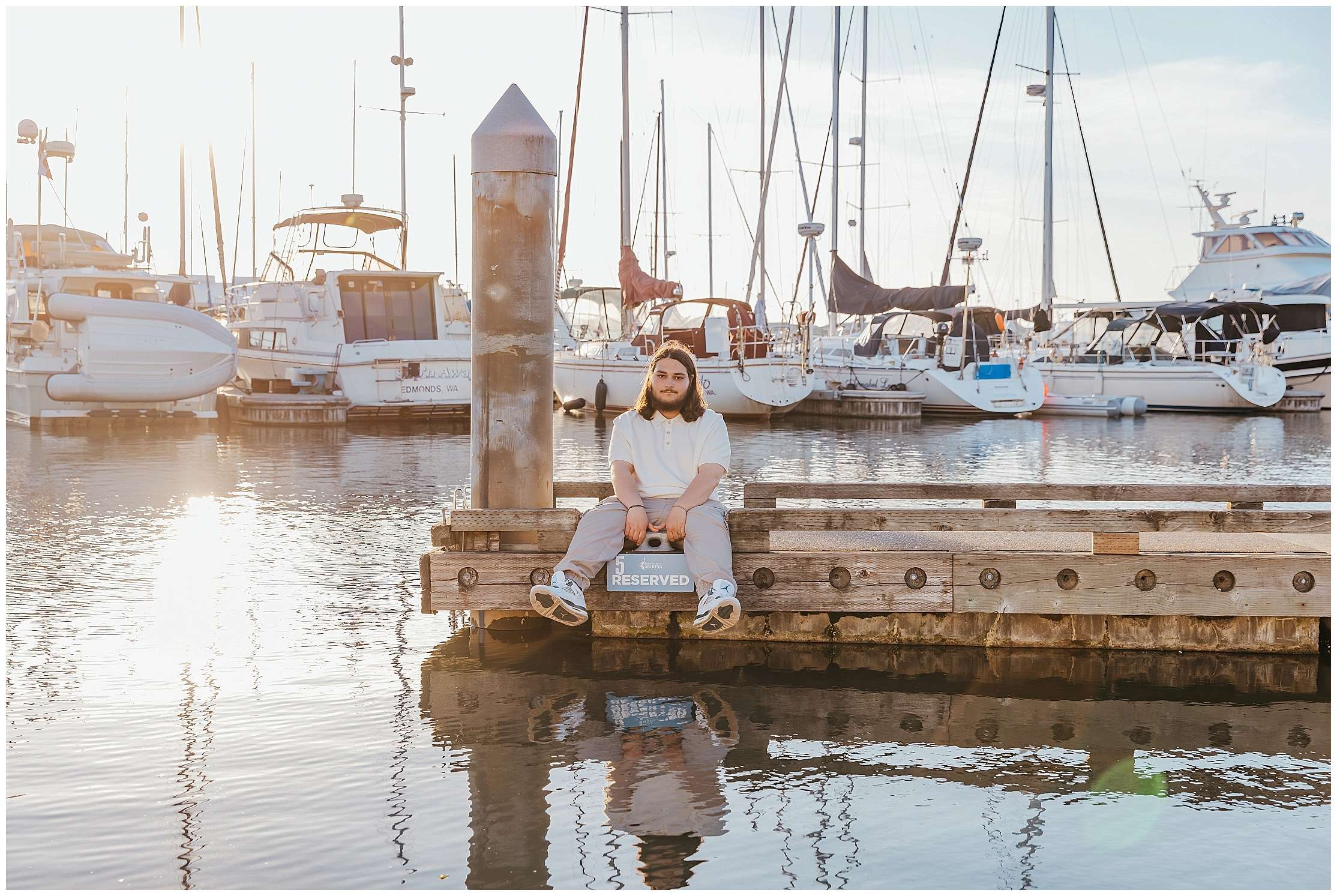 High school senior Nehemiah sitting on a marina dock during golden hour in Everett with sailboats and waterfront views behind him.