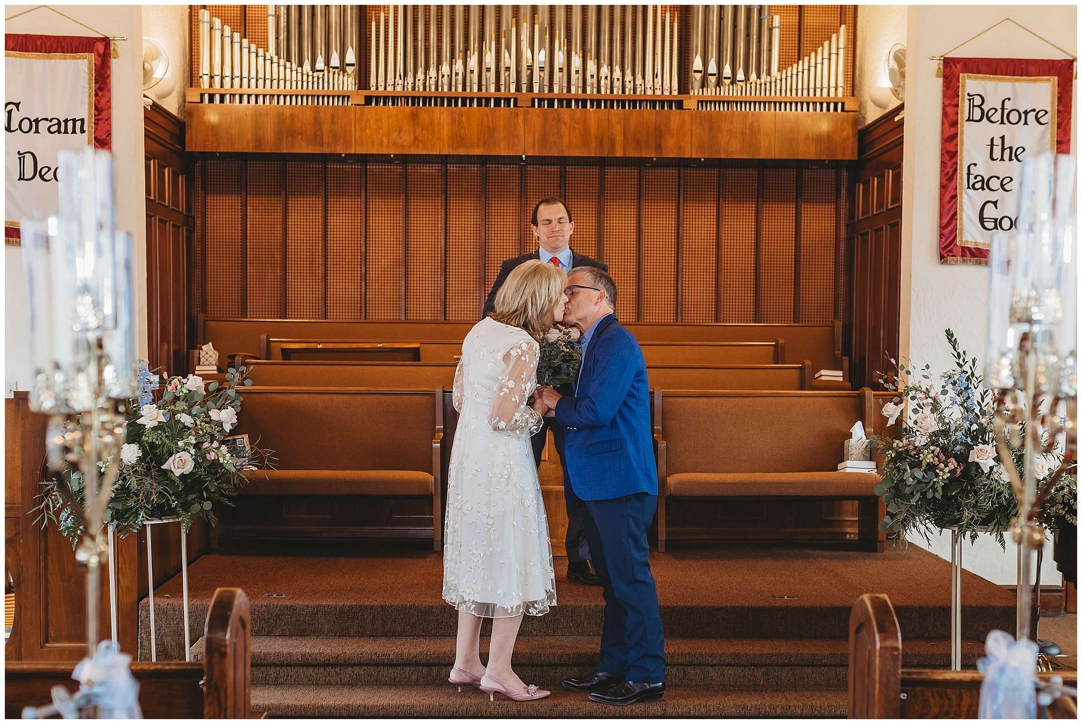 Bride and groom sharing a kiss during their intimate wedding ceremony at Westminster Presbyterian Church in Everett with elegant floral arrangements by Petal and the Stem surrounding the altar.