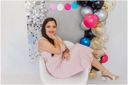 Teen girl posing in a pink sparkly dress during a colorful 15th birthday studio portrait session with bright balloons and a silver disco backdrop in Downtown Everett.