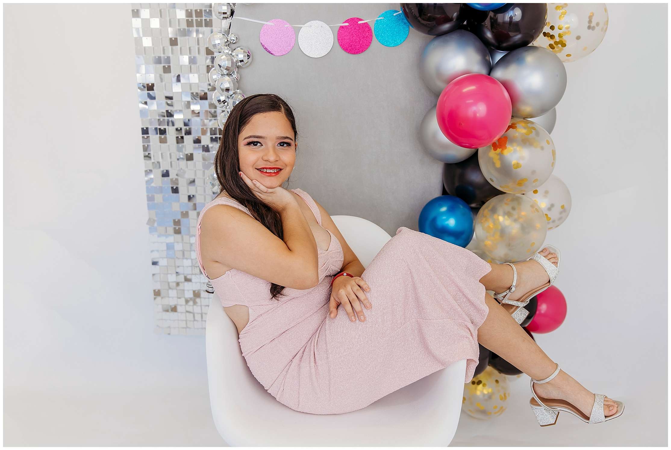 Teen girl posing in a pink sparkly dress during a colorful 15th birthday studio portrait session with bright balloons and a silver disco backdrop in Downtown Everett.